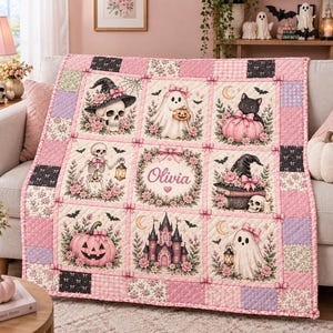 May include: A quilted throw blanket featuring a grid of nine panels with pink, black, and white Halloween-themed illustrations including a skull, ghosts, a black cat, pumpkins, a castle, and the name Olivia centred in a floral wreath.