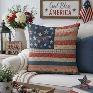 May include: A square throw pillow featuring a patchwork design of the American flag. The left section is a dark blue field with various patterned stars, while the right section consists of horizontal stripes in red, white, and blue floral and plaid patterns.