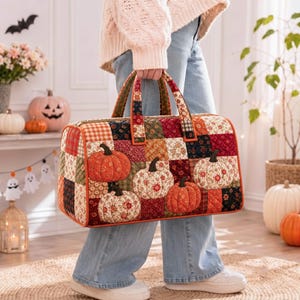 May include: A rectangular quilted duffel bag featuring a patchwork design of autumn-themed fabrics in shades of orange, red, brown, and cream. The bag is decorated with four prominent, three-dimensional fabric pumpkin appliqués.