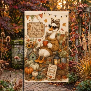 Puede incluir: Una bandera de jardín rectangular que muestra un ganso blanco con una diadema de estampado de leopardo y gafas de sol, sentado en una silla mientras sostiene una taza roja de lunares. La bandera muestra el texto Hello FALL Cozy Days Grateful Hearts y Leaves ARE FALLING AUTUMN IS CALLING, rodeado de calabazas, girasoles y hojas de otoño.