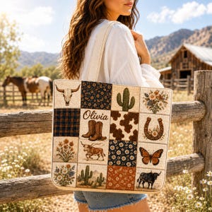 May include: A rectangular tote bag featuring a patchwork design with various western-themed illustrations including a cow skull, cacti, wildflowers, a horseshoe, a butterfly, a bull, and cowboy boots with the name Olivia printed in cursive script.