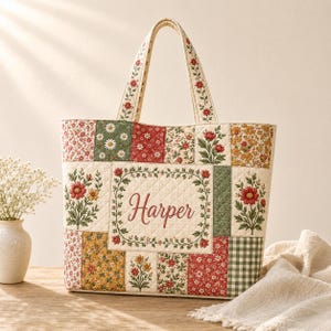 Könnte beinhalten: Eine gesteppte Tragetasche mit einem Patchwork-Design aus Blumenmustern in Rot, Grün, Gelb und Weiß. Das mittlere Feld zeigt den Namen Harper in roter Schreibschrift, umgeben von einem Blumenkranz. Die Tasche hat zwei passende gesteppte Stoffgriffe.