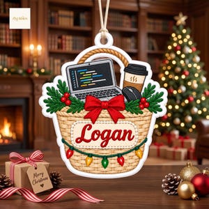 Könnte beinhalten: Ein hängendes Ornament in Form eines geflochtenen Korbs mit einem Laptop, der Code anzeigt, einem Kaffeebecher, einer Computermaus, grünen Tannenzweigen, roten Beeren und einer roten Schleife. Der Korb trägt den Namen Logan und eine Lichterkette.