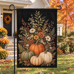 Peut inclure: Un drapeau de jardin rectangulaire sur fond noir, orné d'une illustration centrale de trois citrouilles orange, vertes et blanches, entourées d'un arrangement floral automnal composé de marguerites, de baies et de feuillage séché.