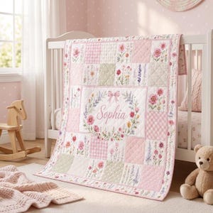May include: A quilted baby blanket featuring a patchwork design of pink gingham, polka dots, and floral patterns. The centre panel displays a floral wreath with a pink bow and the name Sophia printed in cursive script in the middle of the quilt.