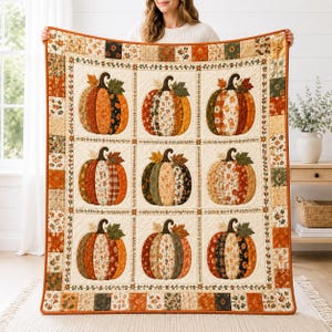 Op de afbeelding: Een rechthoekige quilt met een raster van negen pompoenillustraties, elk samengesteld uit diverse herfstachtige stofpatronen in tinten oranje, bruin, groen en crème. De quilt is omrand door een patchwork van kleine vierkantjes.