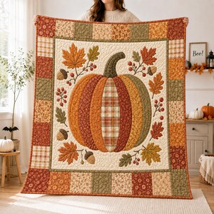 May include: A rectangular quilt featuring a central pumpkin motif surrounded by autumn leaves and acorns. The pumpkin is composed of vertical fabric panels in orange, red, and plaid patterns. The border consists of patchwork squares in autumn colours.