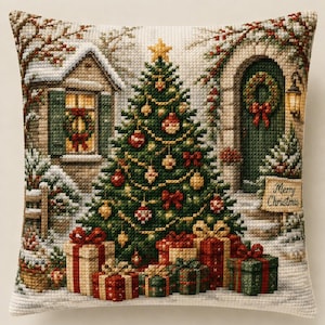 May include: A square throw pillow featuring a detailed cross-stitch design of a decorated Christmas tree, wrapped gifts, and a snowy house exterior. The scene includes a green door with a wreath and a sign that reads Merry Christmas in script.