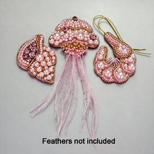 May include: A set of three handcrafted beaded accessories in shades of pink, including a shell-shaped brooch, a jellyfish-shaped brooch with long pink feathers, and a crescent-shaped earring with a gold wire hook. Text reads: Feathers not included.