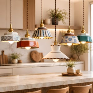 Może przedstawiać: Kolekcja lamp wiszących z ceramicznymi kloszami w różnych kolorach i wzorach. Klosze obejmują niebiesko-białe kwiatowe, paskowe i jednolite wzory. Każda lampa ma mosiężne mocowanie i brązowy przewód, tworząc ciepłą atmosferę.