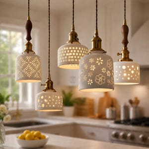 May include: Five pendant lights with white ceramic shades and brass fixtures hang from the ceiling. The shades feature various cut-out patterns, including geometric shapes and floral designs. Each light has a brown wooden accent at the top.