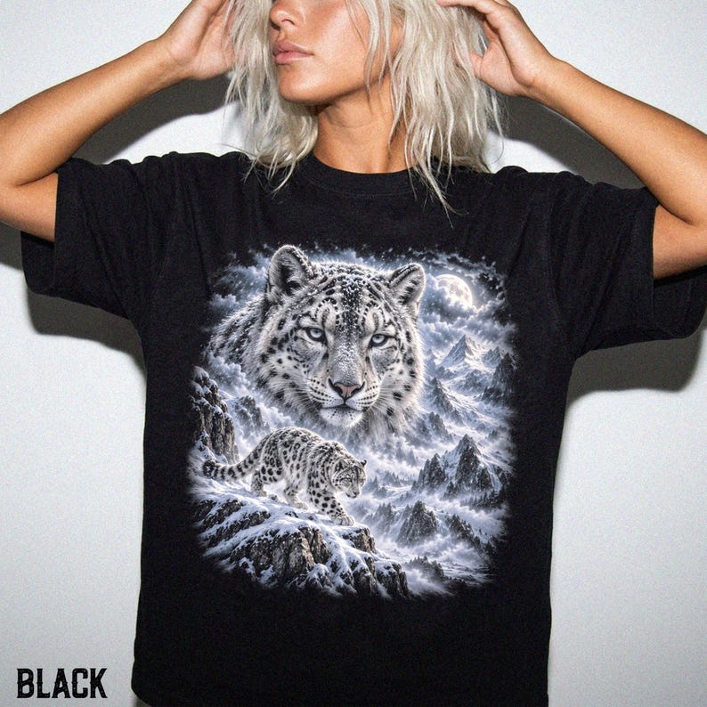 K&ouml;nnte beinhalten: Ein schwarzes T-Shirt mit kurzen &Auml;rmeln und einem gro&szlig;en Grafikdruck eines Schneeleoparden. Das Design zeigt das Gesicht des Leoparden in einer Nahaufnahme &uuml;ber einem kleineren, ganz abgebildeten Leoparden in einer verschneiten Berglandschaft.