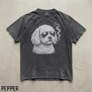 May include: A charcoal grey short-sleeve t-shirt featuring a white graphic illustration of a fluffy dog wearing dark sunglasses and holding a cigarette in its mouth with a trail of smoke rising upwards. The fabric has a faded, washed-out texture.