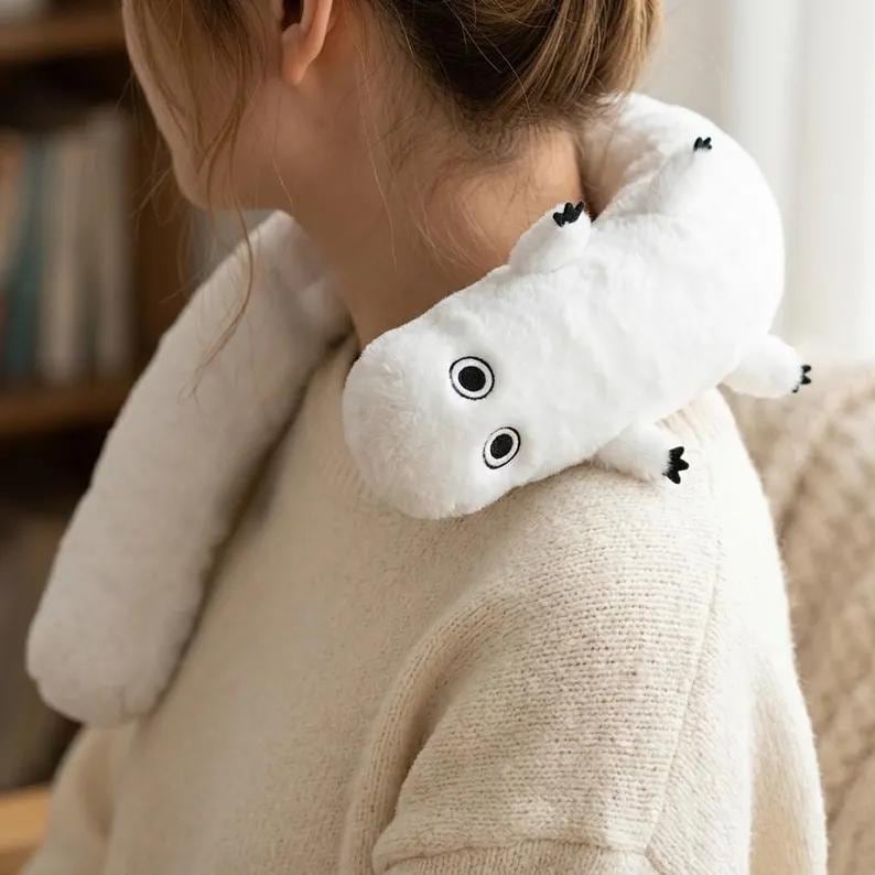Puede incluir: Una almohada de cuello de felpa blanca con forma de gusano o oruga, con ojos negros y peque&ntilde;os pies negros. La almohada est&aacute; dise&ntilde;ada para usarse alrededor del cuello, probablemente para mayor comodidad o relajaci&oacute;n.
