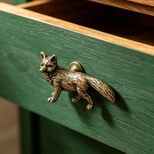 May include: A detailed bronze fox-shaped drawer pull on a green painted wooden drawer. The drawer is open, revealing a natural wood interior. The hardware adds a rustic, animal-themed accent to the furniture.