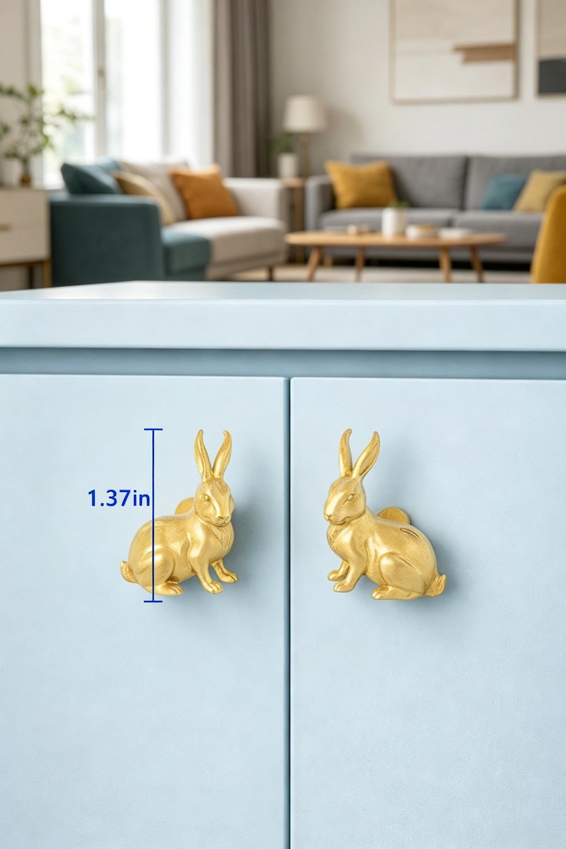 Puede incluir: Dos pomos de armario con forma de conejo de color dorado montados en una puerta de armario azul claro. Cada pomo presenta una figura de conejo detallada en posici&oacute;n sentada. Una l&iacute;nea gr&aacute;fica azul indica una altura de 3,48 cm.