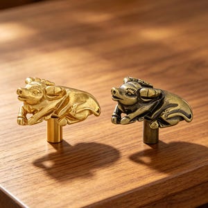 Peut inclure: Deux boutons de placard en forme de buffles d'eau au repos. L'un présente une finition dorée brillante et polie, tandis que l'autre possède une patine en laiton antique plus sombre. Chaque figurine est fixée sur une base cylindrique.