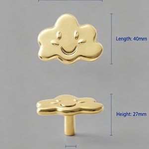 May include: A gold-colored cloud-shaped cabinet knob with a smiling face. The knob has a width of 55 mm, a length of 40 mm, a height of 27 mm, a base width of 8 mm, and a weight of 79 g. The surface is smooth and reflective with a metallic finish.