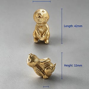 May include: Two gold-coloured metal animal figurines shaped like prairie dogs. One stands upright, the other lies on its side. Dimensions are labelled as 20mm width, 42mm length, 32mm height, 8mm base width, and a weight of 78g for the objects.