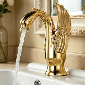 Puede incluir: Un grifo de baño en tono dorado pulido con forma de cisne y texturas detalladas de alas en los laterales. El cabezal del grifo está posicionado como el cuello y la cabeza del cisne, con agua fluyendo constantemente desde el pico hacia un lavabo de cerámica.