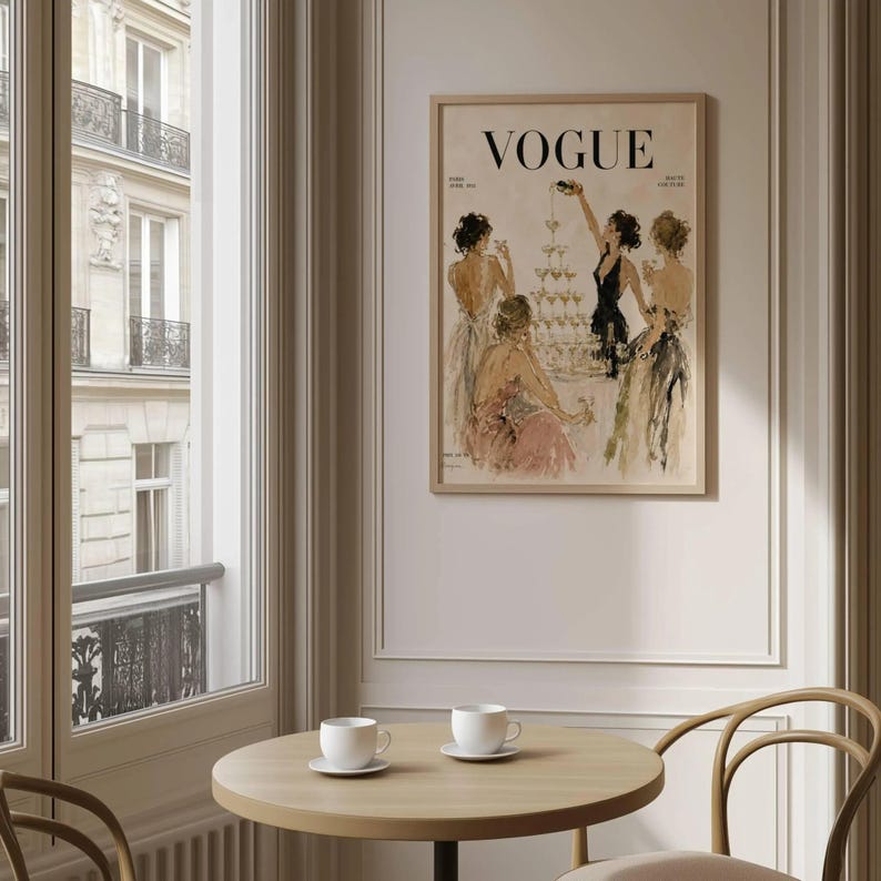 May include: A framed print of a Vogue magazine cover, showcasing an illustration of women in evening gowns, celebrating with champagne. The print has a vintage style, with the Vogue logo at the top. The print is displayed in a room with a round table and two teacups.