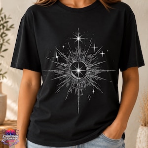 May include: A black short-sleeved t-shirt featuring a white graphic print of a central circular orb surrounded by radiating starburst lines and smaller four-pointed stars. The design is positioned on the chest area of the garment.