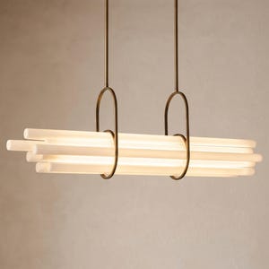 May include: A linear pendant light fixture featuring a rectangular bronze-toned ceiling mount with two vertical rods supporting two oval-shaped bronze loops. These loops hold a cluster of horizontal, frosted white cylindrical glass light tubes.