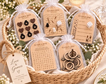 Puede incluir: Cinco pequeñas bolsas de organza blanca con tableros de juego de madera con el texto ELYSSA & GENE July 25 2026. Los juegos incluyen tres en raya, un tablero numerado con dados, un juego de beber, una sopa de letras y aros. Una etiqueta dice Love & Games.