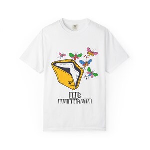 May include: White t-shirt with a graphic of a yellow wallet and colorful butterflies. The text "DAD: WALKING ATM" is printed below the wallet. The shirt is a casual style.