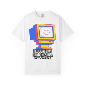 May include: White t-shirt with a colourful retro computer graphic. The screen displays a smiley face. Text below the graphic reads, "I KEEP ALL MY DAD JOKES IN A DAD-A-BASE."