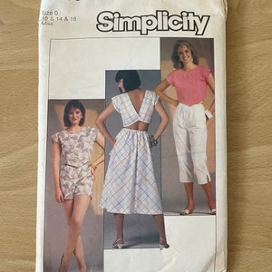 May include: Simplicity sewing pattern number 6853 for sizes 12, 14, and 16. The pattern includes three different outfits: a white top with a plaid skirt, a pink top with white trousers, and a floral print top with shorts.