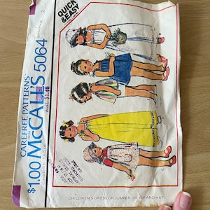 May include: A vintage McCall's sewing pattern for children's clothing. The pattern is for a dress, jumper, or top and hat. The pattern is numbered 5064 and is priced at £1.00. The pattern features illustrations of four girls wearing the different garments.