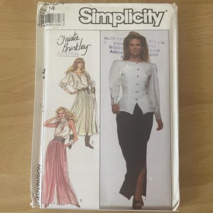 Op de afbeelding: Een vintage Simplicity naaipatroon met ontwerpen uit de Christie Brinkley Collection. De patroonverpakking toont illustraties van een witte blouse, zwarte rok en andere elegante kledingstukken. Maat 14.