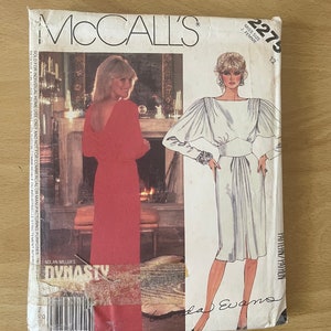 Könnte beinhalten: Ein Vintage-Schnittmuster von McCall's für ein Kleid, mit einem weißen Kleid mit Puffärmeln und einem roten Kleid mit tiefem Rücken. Das Schnittmuster ist mit "Miss Size J. Femme" und "2275" gekennzeichnet. Das Schnittmuster ist für ein Kleid aus der Fernsehserie "Dynasty" von Nolan Miller.