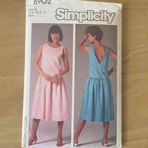 Könnte beinhalten: Simplicity Schnittmuster 6902. Das Muster zeigt zwei Kleiderdesigns. Ein Kleid ist rosa und weiß gestreift, das andere hellblau. Die Mustergröße ist N, 10, 12 und 14.