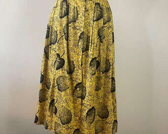 May include: A yellow maxi skirt with a black leaf print and button closure. The skirt is pleated and has a high waist.