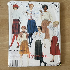 May include: McCall's pattern 2147 for skirts in sizes 10-12-14. The pattern includes instructions for three different skirt styles. The pattern cover features a model wearing a red plaid skirt, a model wearing a blue plaid skirt, and a model wearing a brown skirt.