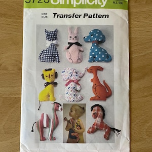 Könnte beinhalten: Simplicity Transfermuster 5723 mit verschiedenen Stofftierdesigns. Das Muster beinhaltet eine Katze, ein Kaninchen, einen Hund, einen Löwen, einen Elefanten, ein Känguru, ein Kamel und ein Pferd. Das Muster ist Einheitsgröße.