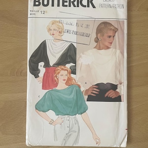 May include: A vintage Butterick sewing pattern, size 12, featuring illustrations of blouses. The cover has the text "Butterick" and "Pattern/Patron". The illustrations show different blouse styles in black, white, red, and teal.