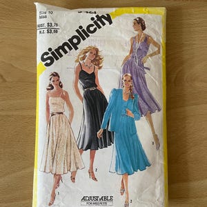 May include: Simplicity sewing pattern envelope for size 10 miss. The envelope features three different dress designs: a black dress with a white belt, a white and brown gingham dress, and a blue dress with a matching jacket. The text "ADJUSTABLE FOR MISS PETITE" is printed on the envelope.