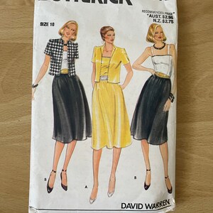 Op de afbeelding: Een vintage naaipatroon envelop voor een damesjurk en jas. Het patroon is van Butterick en is maat 10. De envelop toont drie illustraties van vrouwen die de kledingstukken dragen. De jurk is een gele rok met een wit topje en een zwart jasje. Het jasje wordt ook getoond met een zwart-wit geruit topje en een zwarte rok. Het patroon is voor een rok met een brede tailleband.