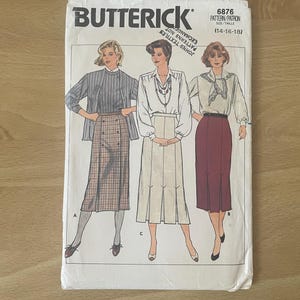 May include: A vintage Butterick sewing pattern envelope. The cover features illustrations of three women modeling different outfits, including skirts and blouses. The pattern number is 6876, and the size range is (14-16-18).