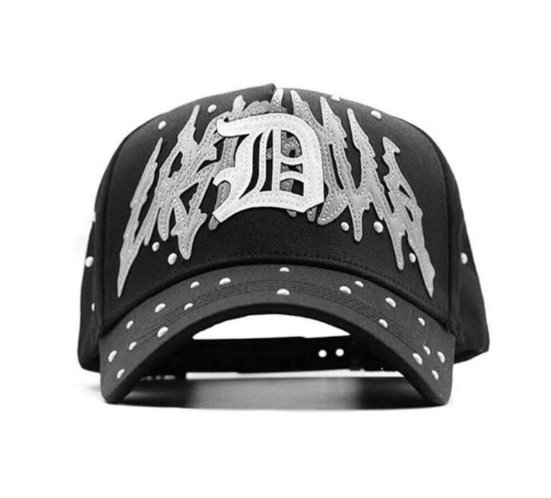 May include: Black baseball cap with white text and accents. The cap features the word "URBAN" in a stylized font, with a large "D" in the center. White dots are on the brim and around the cap.