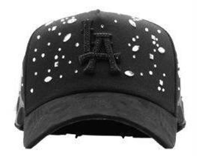 May include: Black baseball cap featuring the letters "LA" embroidered on the front. The cap is adorned with white and silver embellishments. The brim is curved, and the cap has a classic six-panel design.