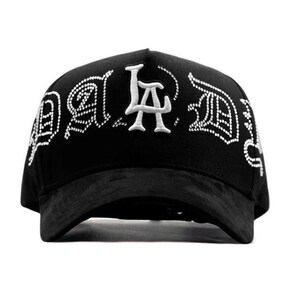 May include: Black baseball cap with white embroidered text that reads "LA" in a stylized font. The cap has a curved brim and a structured crown. The text is outlined with small white dots. The cap is made of a soft material.