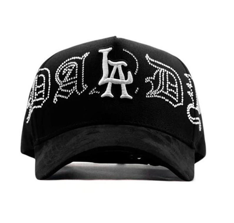 May include: Black baseball cap with white embroidered text that reads "LA" in a stylized font. The cap has a curved brim and a structured crown. The text is outlined with small white dots. The cap is made of a soft material.