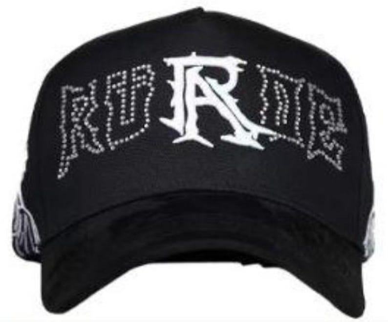 May include: Black baseball cap with the word "RURE" in white, embellished with rhinestones. The brim is black, and the cap has a curved visor. The cap is a stylish accessory.