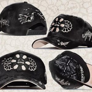May include: A black baseball cap featuring white embroidered graphics of a sad flower with stitched mouth, stars, and hand motifs. The cap has a structured crown, a curved brim with a light-colored underside, and an interior lining with text.