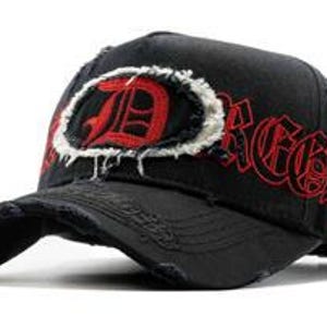 May include: Black baseball cap with a distressed brim and a large, red letter "D" inside a white, frayed oval. The word "Dread" is embroidered in red on the side. The cap has a worn, vintage appearance.