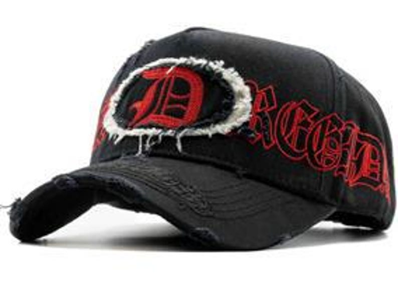 May include: Black baseball cap with a distressed brim and a large, red letter "D" inside a white, frayed oval. The word "Dread" is embroidered in red on the side. The cap has a worn, vintage appearance.